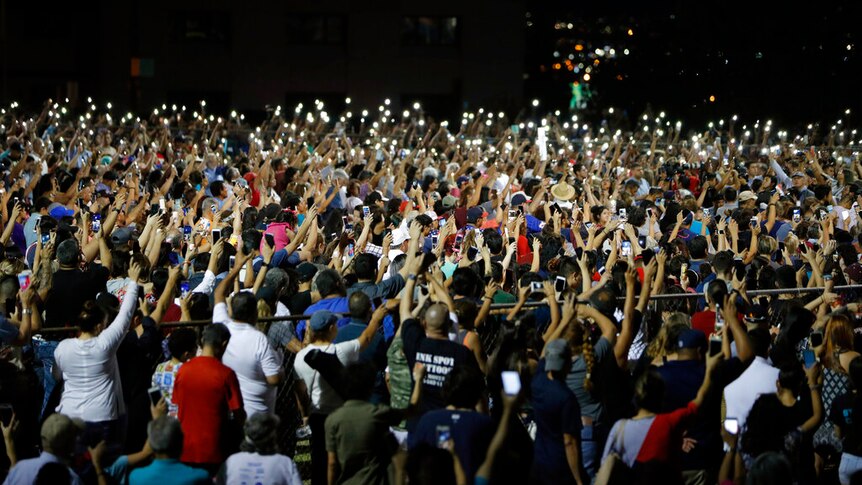 A large group of people standing with their hands in the air, holding candles