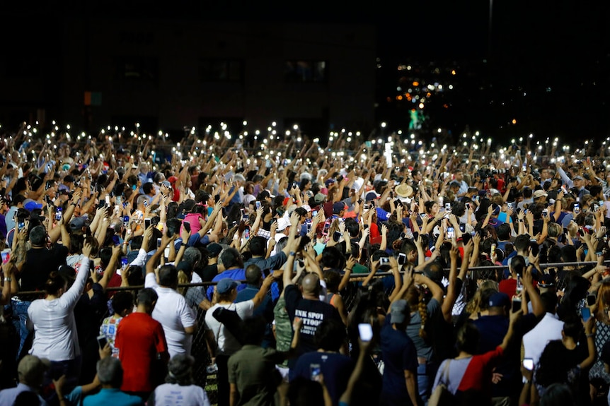 A large group of people standing with their hands in the air, holding candles