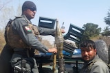 Afghan police ride on the back of a truck, holding guns.