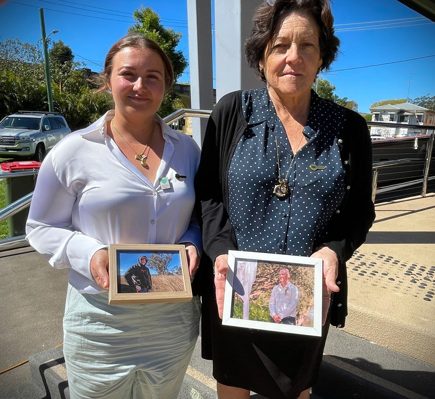 Two women holding photographs in front of hundreds of shoes representing road deaths.