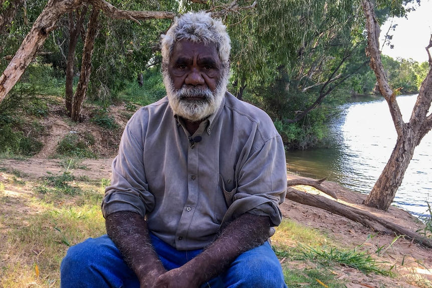 Garawa Elder Jack Green sits by a river, he has a beard and white hair.