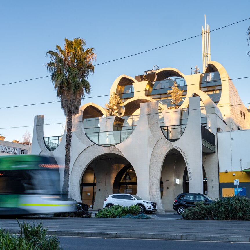 The protruding concrete tubes of the Victorian Pride Centre is seen between trams on 