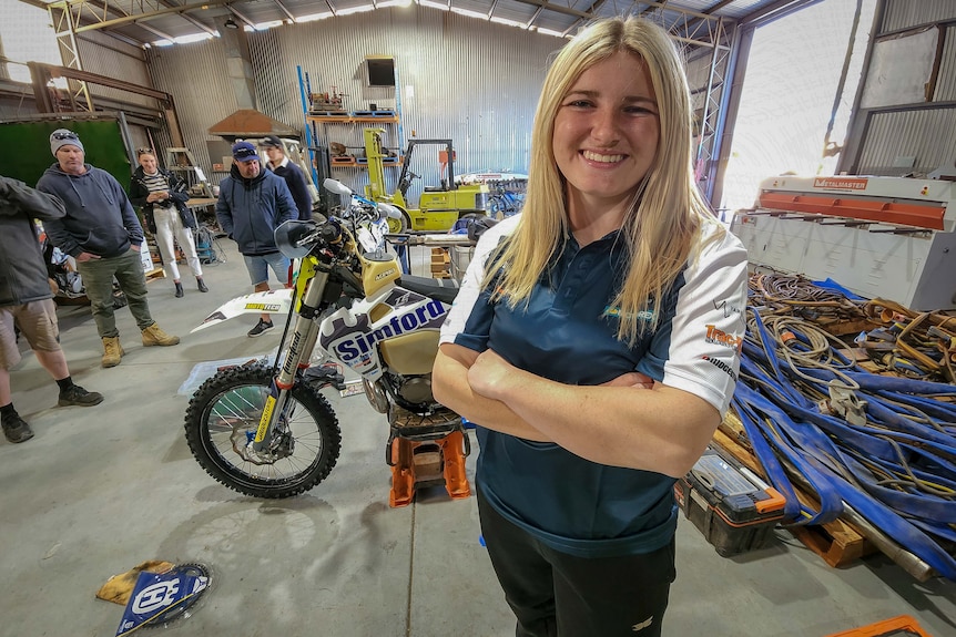 smiling blonde girl in shed with dirt bike behind her