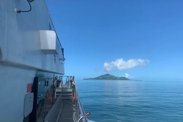 the side of a large boat on the ocean with a tropical island behind
