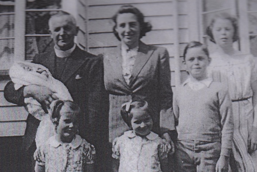 man holds baby and stands with woman and young children