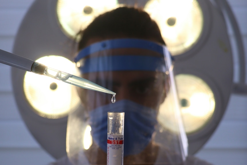 A surgeon wearing a plastic face mask and scrubs refills an injection with vaccines