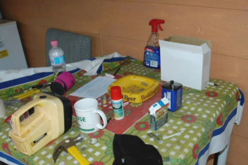 A table with a number of items on it, including a torch, coffee mug, cigarette packet, stubby holder and hammer.