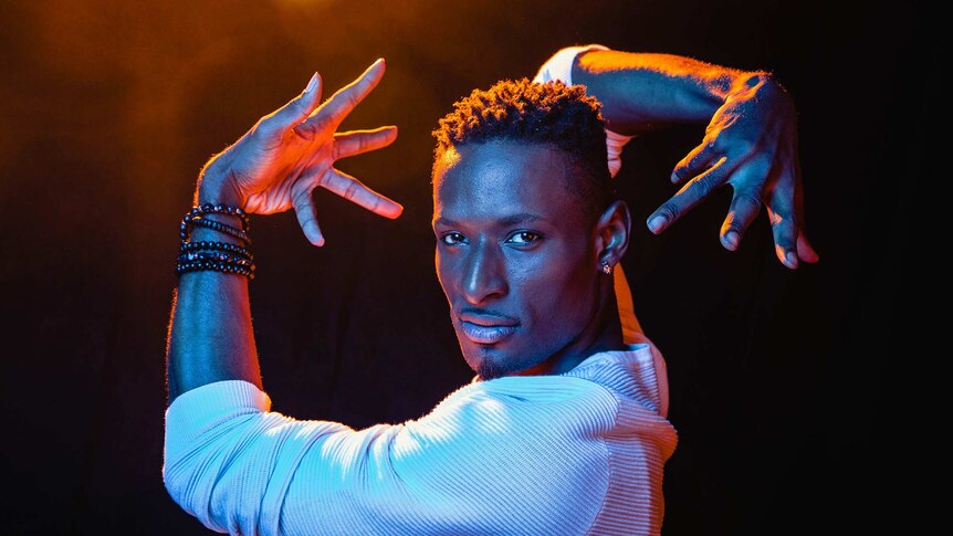 A dramatic colour close-up photo of Dashaun Wesley in a dance pose in front of dark background.