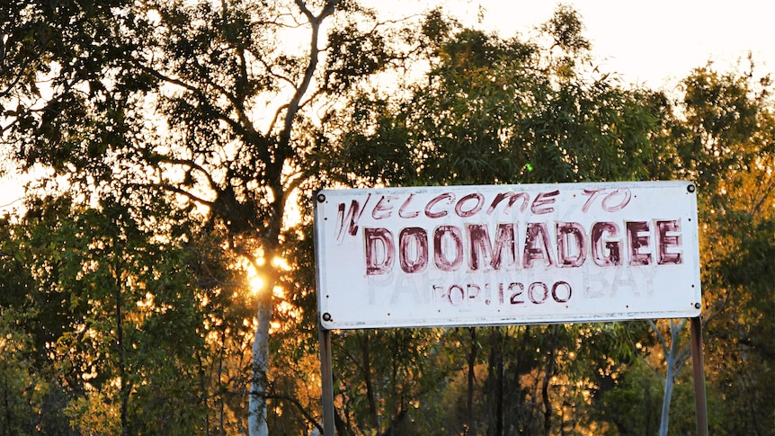 An old weathered sign that reads Welcome to Doomadgee with a bush setting behind it