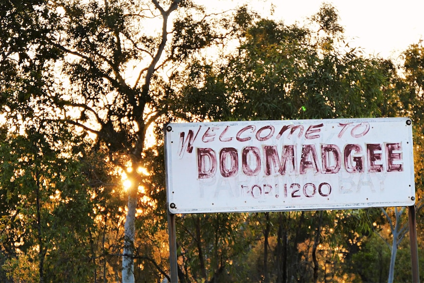 An old weathered sign that reads Welcome to Doomadgee with a bush setting behind it