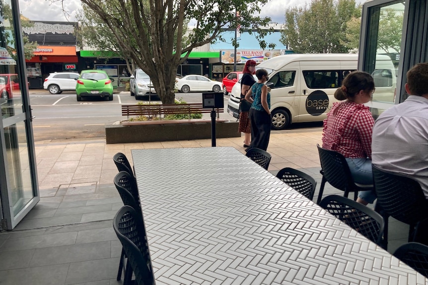 An empty outdoor dining table in a Toowoomba street, with people standing on the footpath and seated nearby.