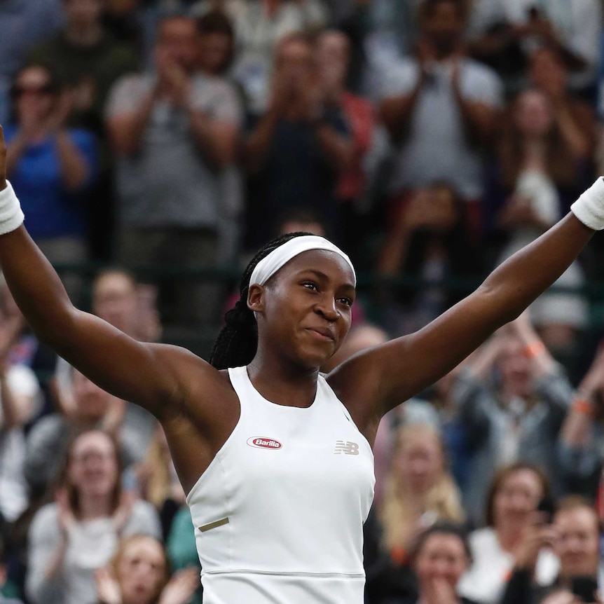 A girl on a tennis court smiling with her arms outstretched