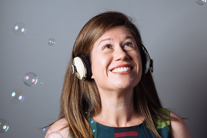 Addie Wootten, smiling while wearing headphones, looking up surrounded by bubbles