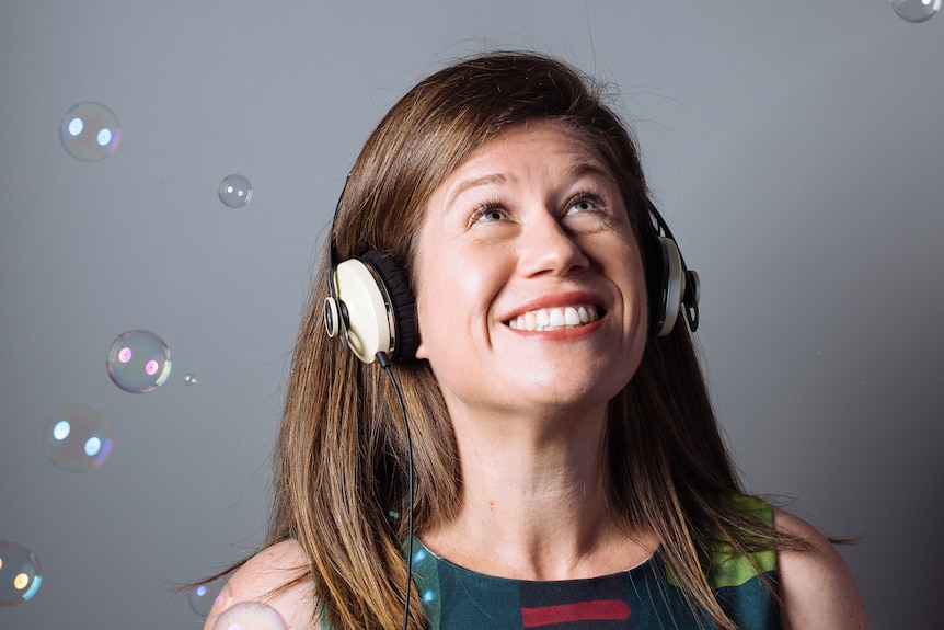 Addie Wootten, smiling while wearing headphones, looking up surrounded by bubbles