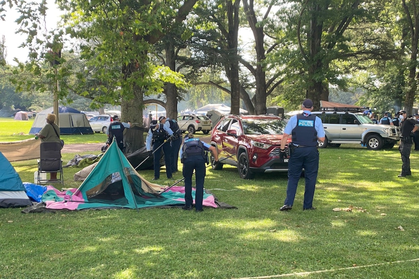 Uniformed police take apart a tent.
