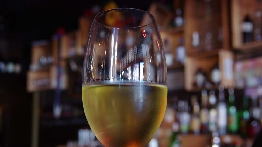 A wine glass containing white wine sitting on a bar.