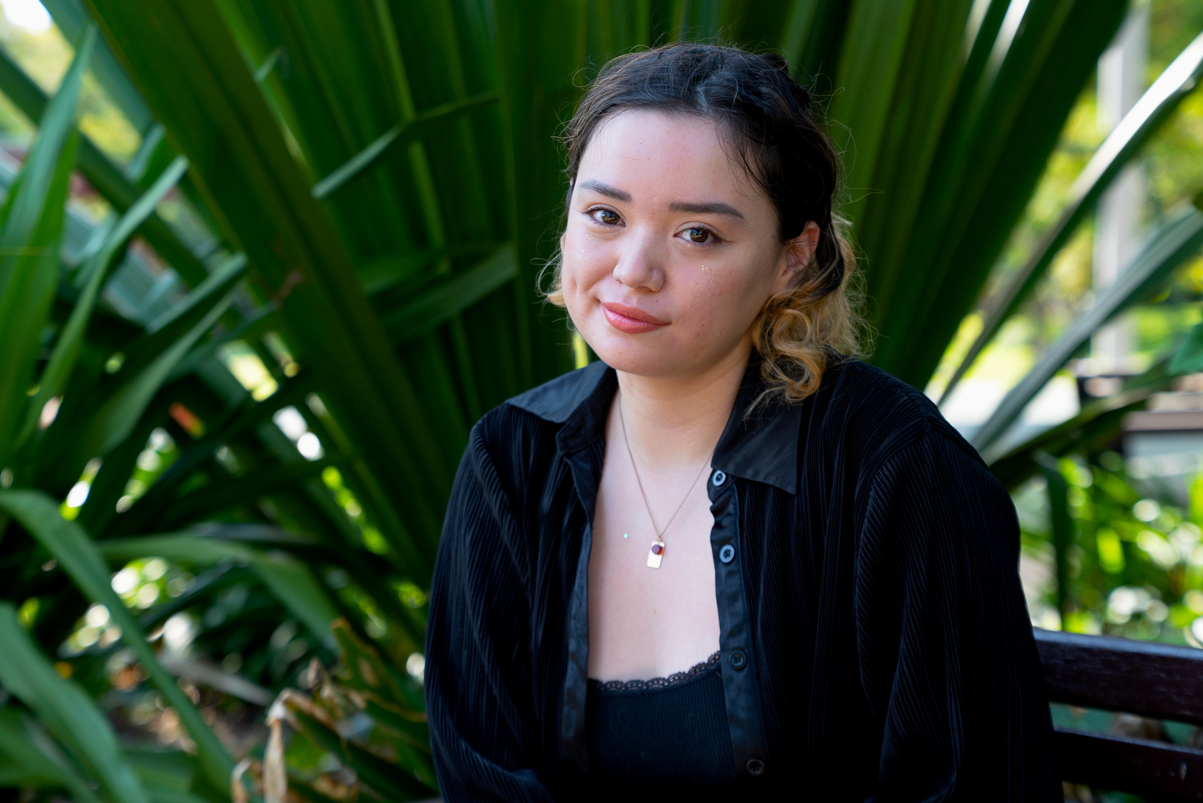 A young woman in a black shirt in front of plants. 