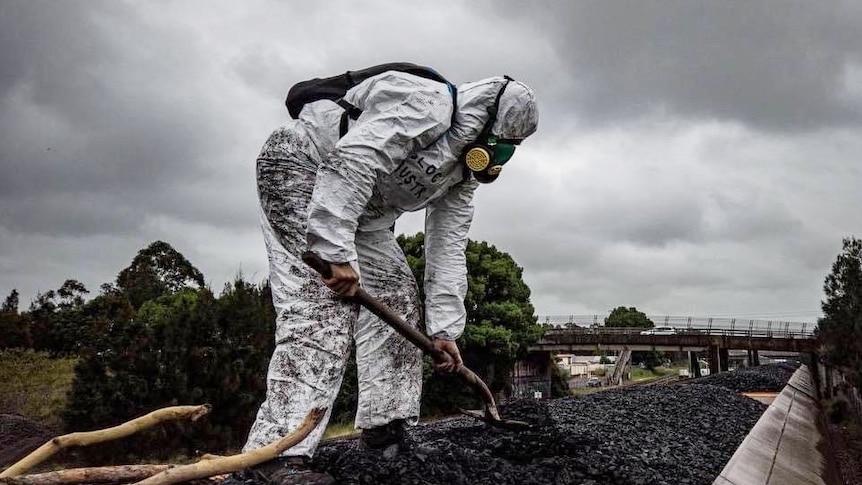 a perosn in white overalls and has mask shovels coal on the top of a coal wagon 