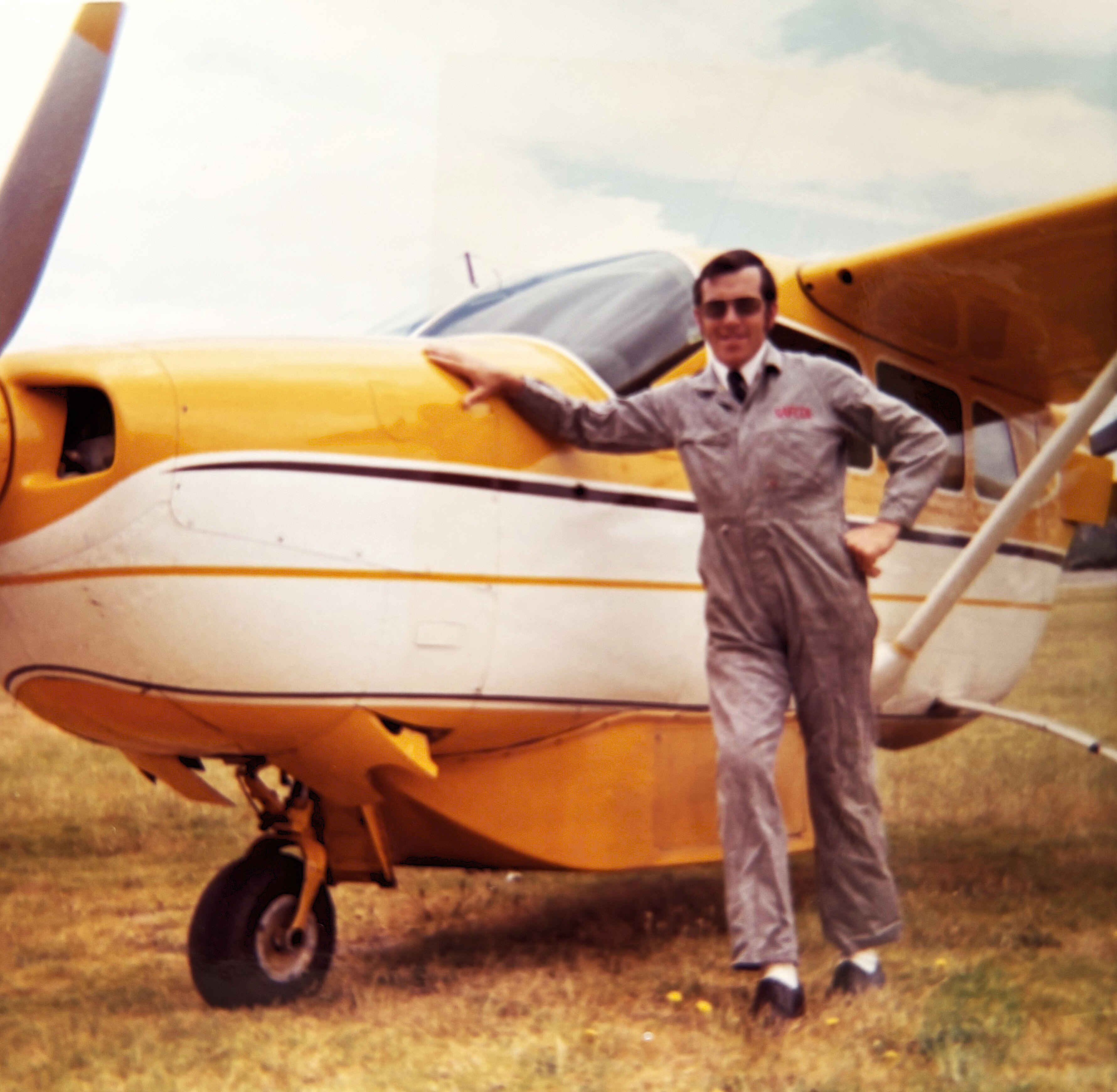 Man in overalls and glasses in front of small yellow and white plane with wing above the cabin.