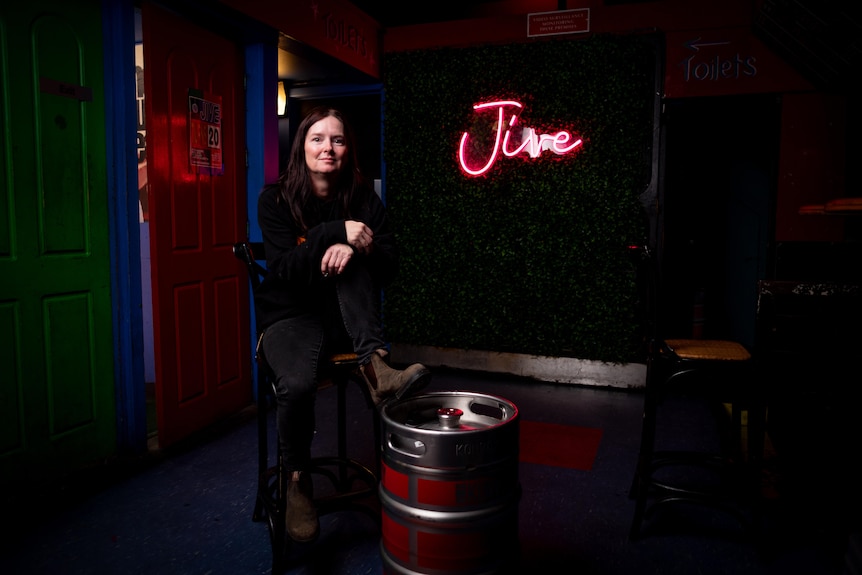 A woman sits in a dark bar, one feet propped up on a beer tank