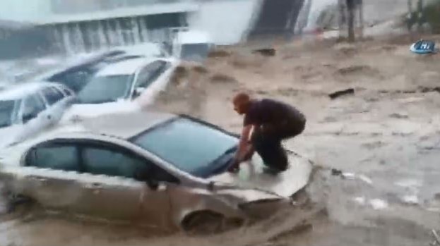 Man crouches and surfs on the hood of his car during flooding in Ankara, Turkey.