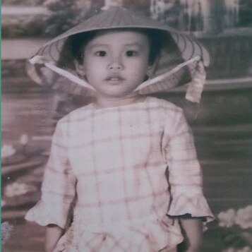 A black and white photo of a young girl wearing a Vietnamese pointed hat.