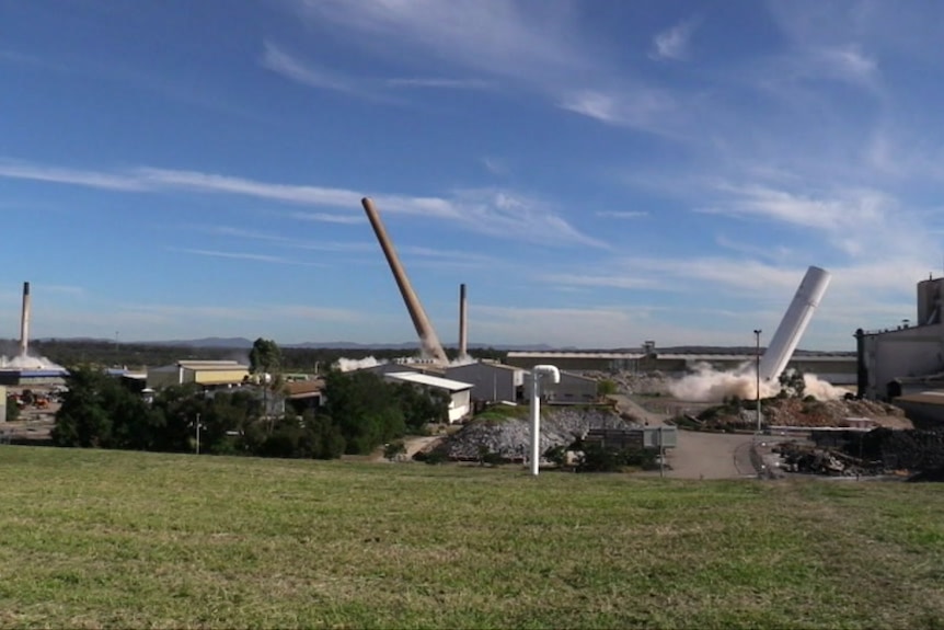 Four smoke stacks lean over after explosives are used to bring them to the ground.