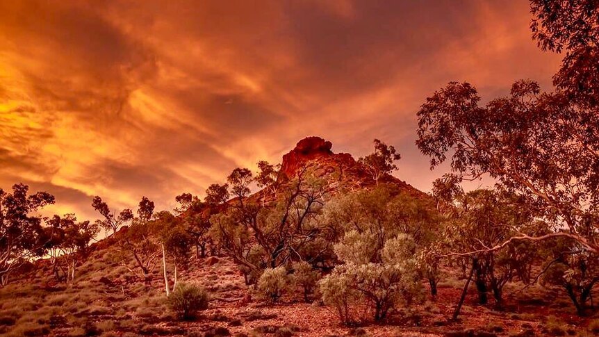 An orange sunset surrounds a rocky outcrop.
