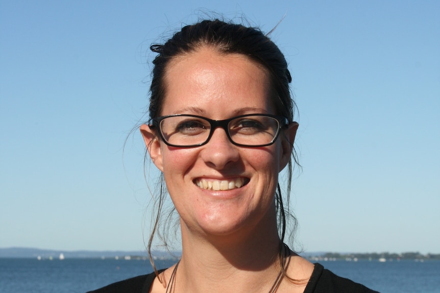 A lady with glasses smiling at the beach.