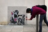 A man takes a photo of an artwork attributed to Banksy on the side of a discount shop in north London.