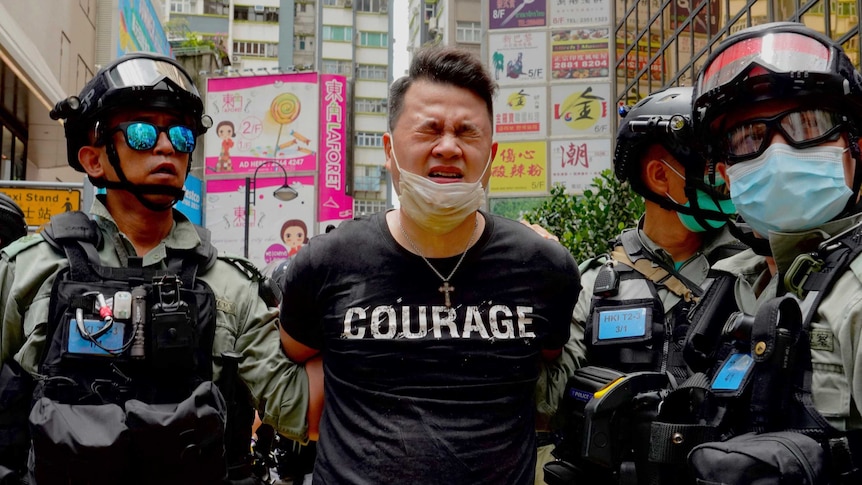 Police detain a protester after being sprayed with pepper spray during a protest in Hong Kong. His t-shirt reads "courage".