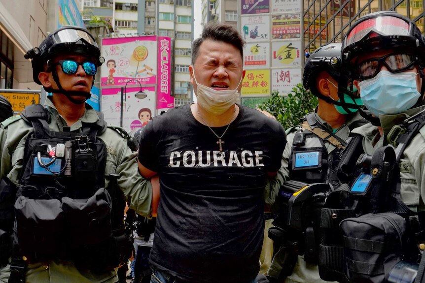 Police detain a protester after being sprayed with pepper spray during a protest in Hong Kong. His t-shirt reads "courage".