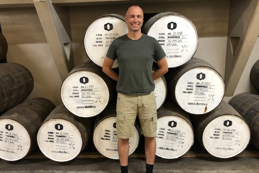Dawid Ostrowski stands in front of some barrels inside his distillery.