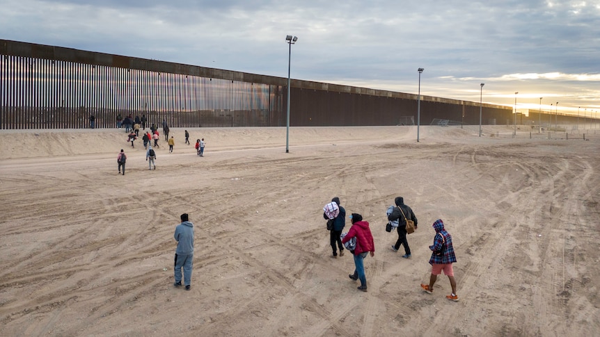 migrants walking to section of US-Mexico border wall
