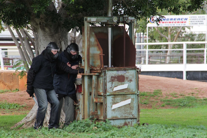 Two police dressed in black clothes and helmets hide behind a metal contraption during a counter-terrorism exercise.