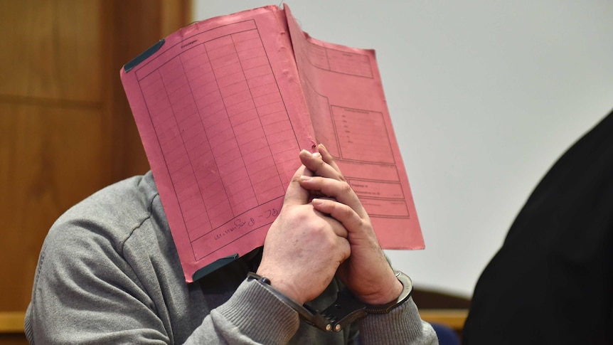 Niels H attempts to cover his face with a red file in court in 2015