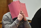 Niels Hoegel attempts to cover his face with a red file in court in 2015