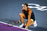 Aryna Sabalenka kneels and touches the court during a tennis match against Maria Sakkari.