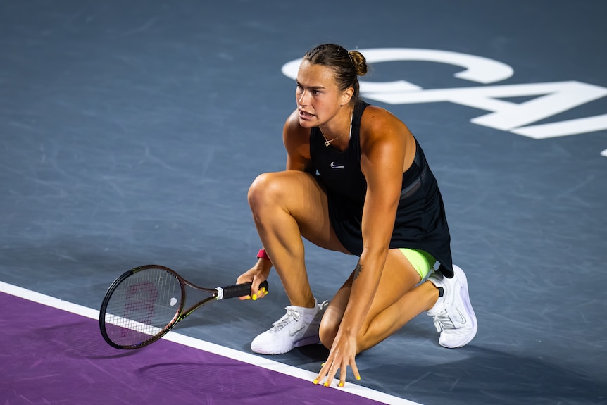 Aryna Sabalenka kneels and touches the court during a tennis match against Maria Sakkari.