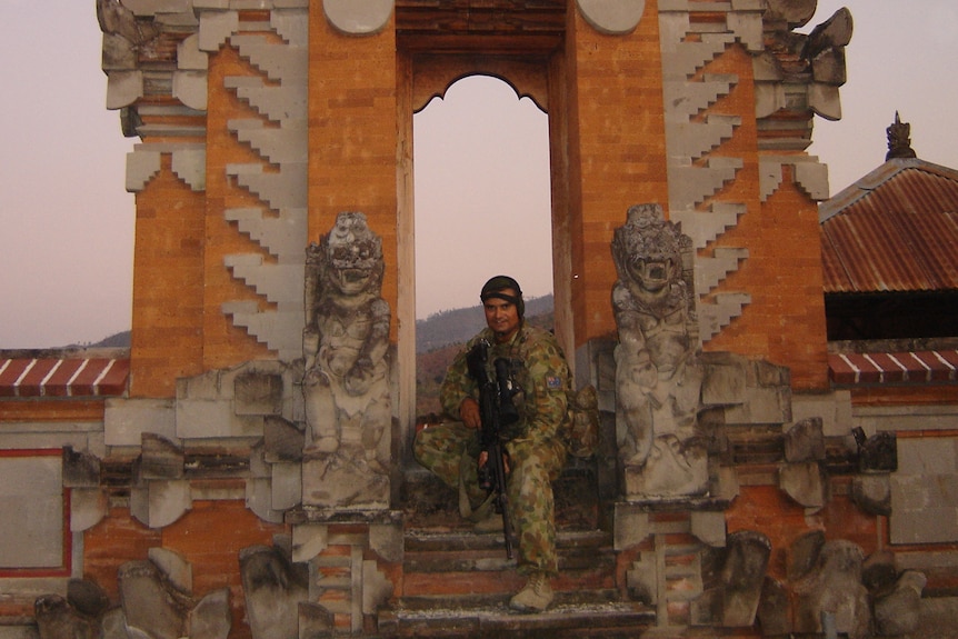 A soldier poses for a photo on the steps of what appears to be a temple with a nice sky in the background.