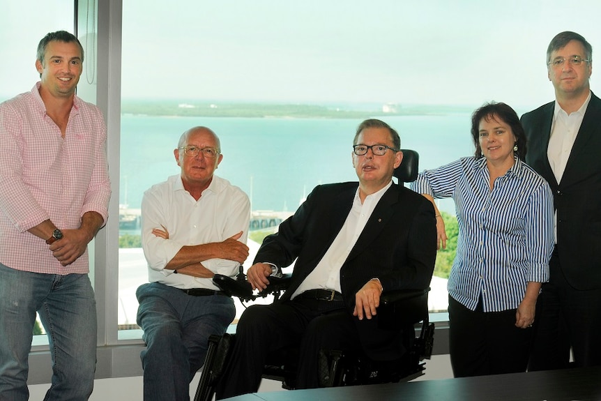 The five board members stand in an office, with a sea view behind them