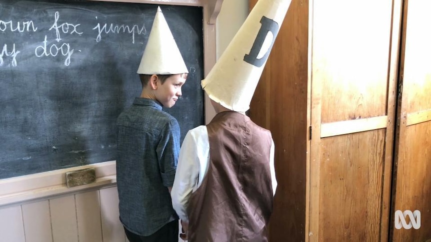 Children wear dunce hat while standing in corner of classroom