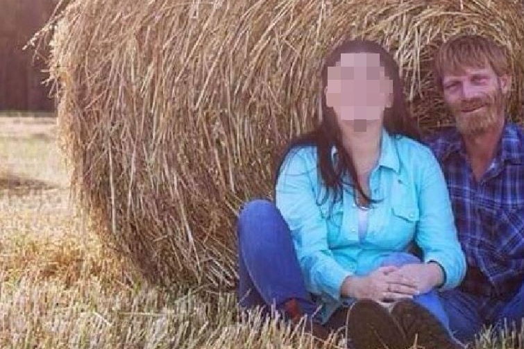Peter Moiler sits beside a woman whose face is pixellated in front of a hay bale