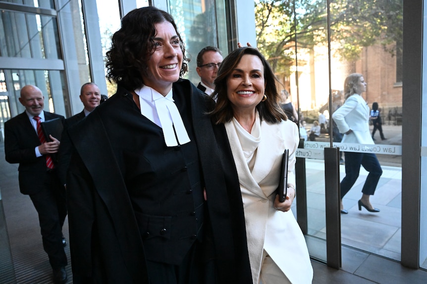Una mujer con traje blanco sonríe, en brazos de un abogado.