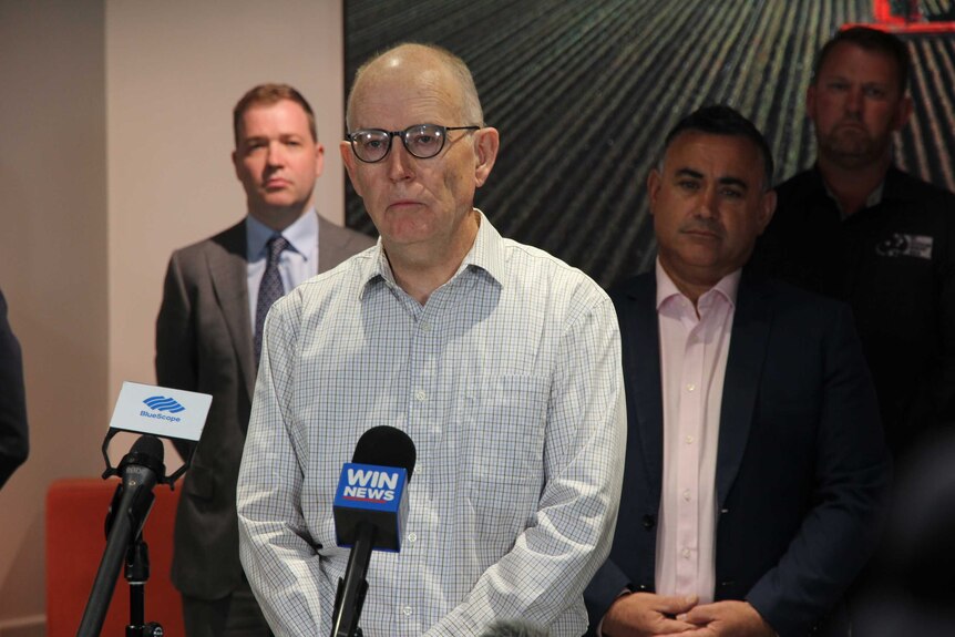 Man stands in front of microphone talking to the media