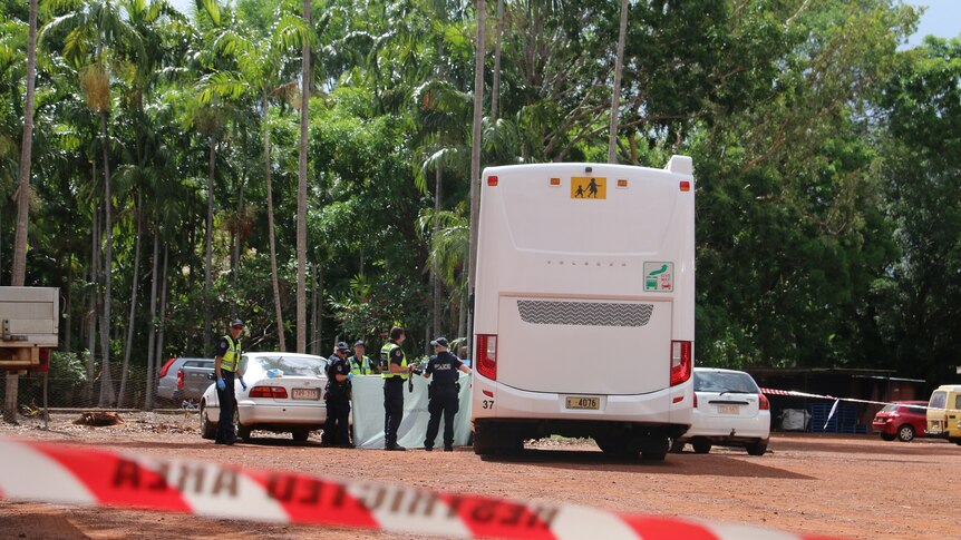 Police tape cordons of a section of carpark with police holding up a sheet