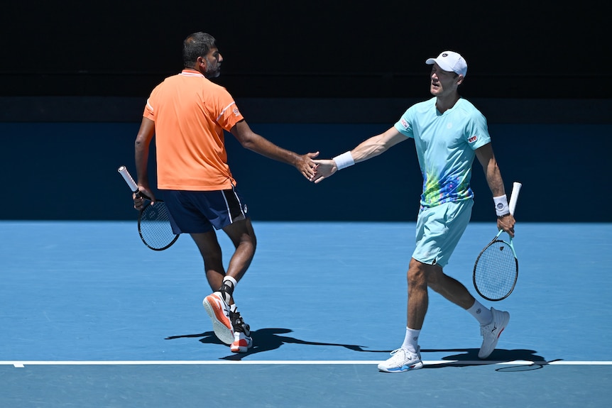 Two men's doubles player shake hands as they celebrate winning a point.