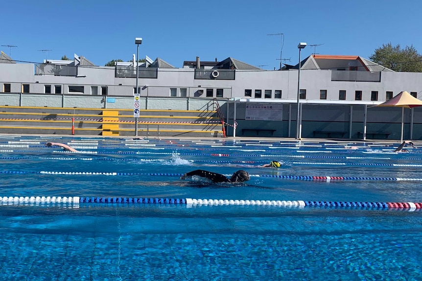A person swims laps wearing a wetsuit in an outdoor pool.