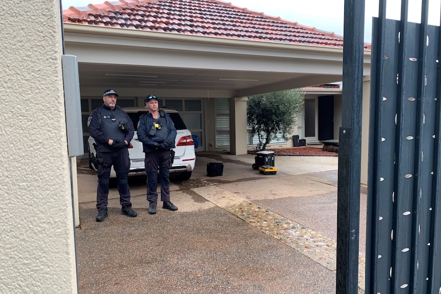 Two police officers standing under a carport with a Mercedes four-wheel drive under it