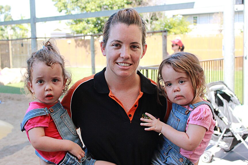 Woman holds twin toddlers in each arm